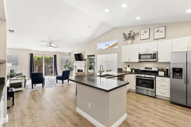 kitchen featuring visible vents, appliances with stainless steel finishes, dark countertops, a sink, and a warm lit fireplace