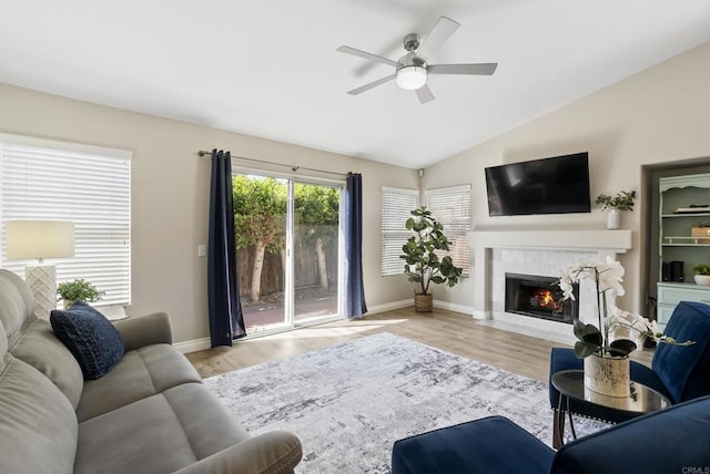 living room featuring a ceiling fan, baseboards, a fireplace with flush hearth, wood finished floors, and vaulted ceiling