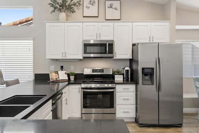 kitchen featuring dark countertops, appliances with stainless steel finishes, white cabinets, and a sink
