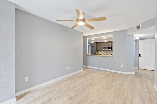 empty room with a sink, a ceiling fan, baseboards, wood finished floors, and visible vents