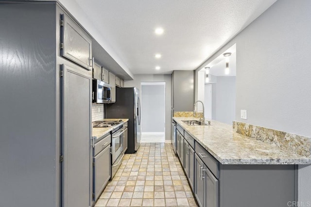 kitchen featuring a peninsula, recessed lighting, gray cabinets, a sink, and stainless steel appliances