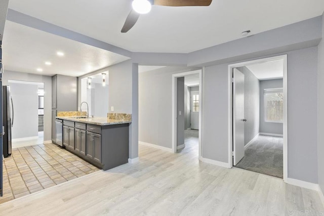 kitchen with a ceiling fan, baseboards, a sink, light wood-style flooring, and stainless steel appliances