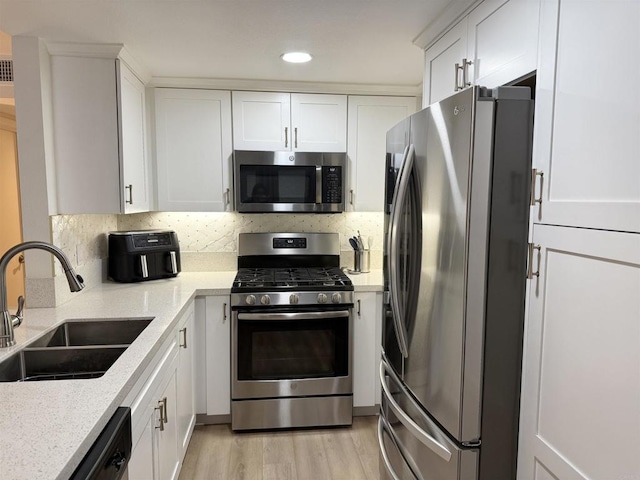 kitchen with white cabinets, a sink, stainless steel appliances, recessed lighting, and light wood-type flooring