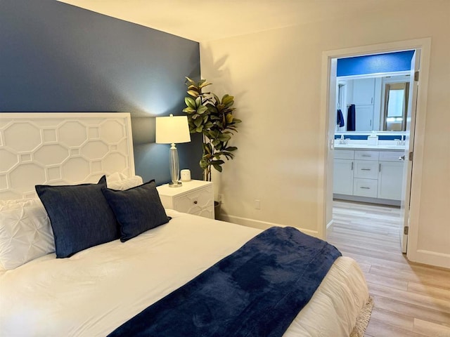 bedroom with connected bathroom, baseboards, a sink, and light wood-style floors