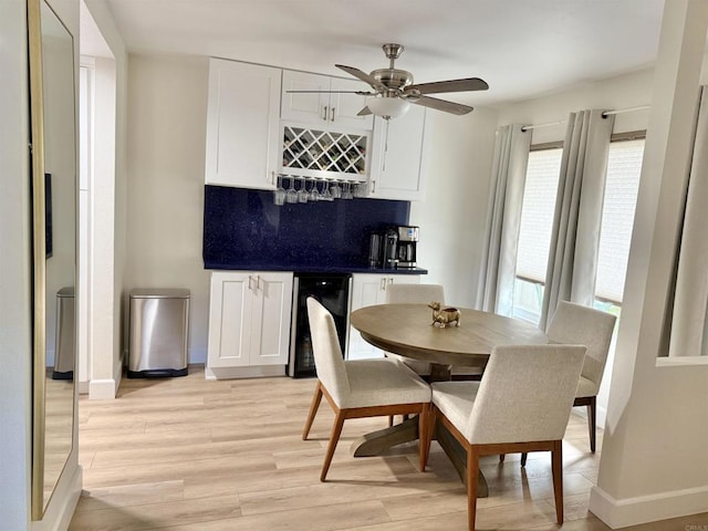 dining area featuring ceiling fan, beverage cooler, light wood-style flooring, baseboards, and a bar