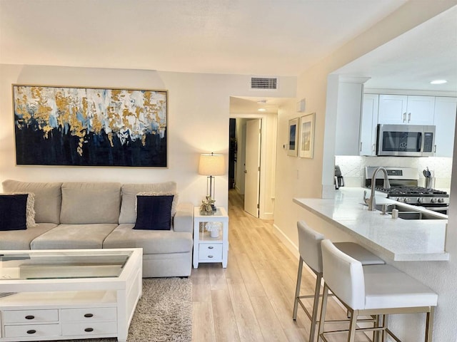 living area featuring visible vents, light wood-style flooring, and baseboards