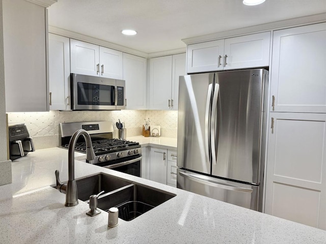 kitchen featuring light stone countertops, white cabinets, a sink, backsplash, and stainless steel appliances