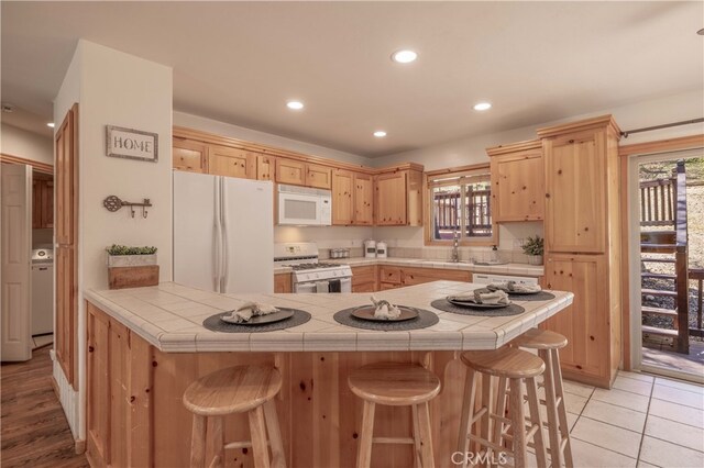 kitchen with a peninsula, light brown cabinets, white appliances, a kitchen breakfast bar, and tile counters
