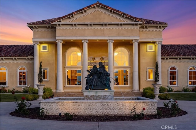 exterior entry at dusk featuring a porch, stucco siding, and a tiled roof