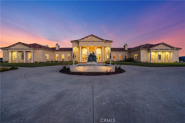 mediterranean / spanish house featuring curved driveway, stucco siding, and a chimney