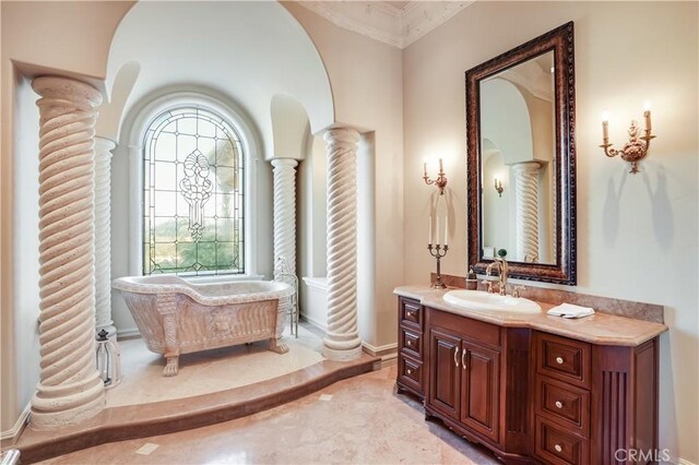 bathroom with vanity, ornamental molding, decorative columns, baseboards, and a soaking tub