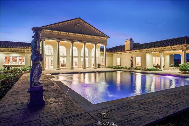 back of property with a patio, an outdoor pool, stucco siding, and a chimney