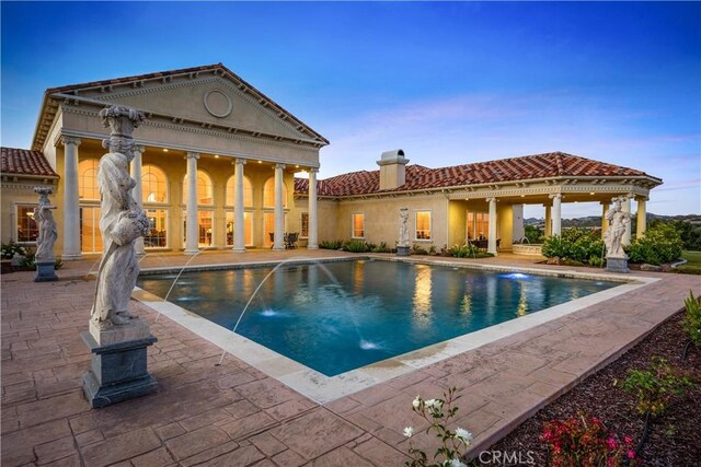 rear view of property featuring a tile roof, stucco siding, an outdoor pool, a chimney, and a patio area