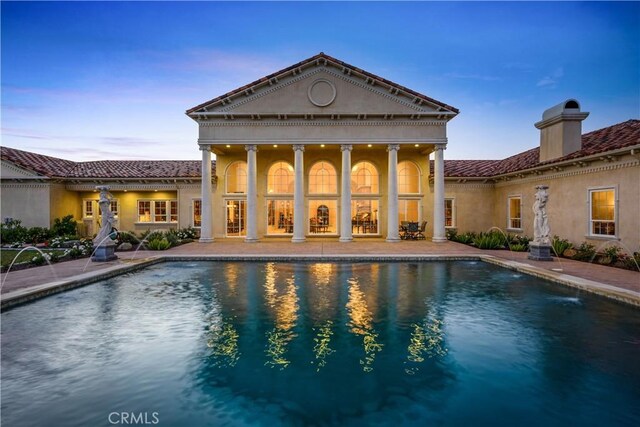 back of property at dusk featuring a chimney, an outdoor pool, a patio area, and stucco siding