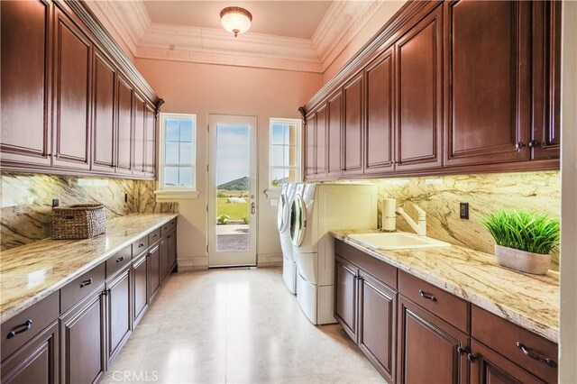 washroom with cabinet space, crown molding, washing machine and dryer, and a sink
