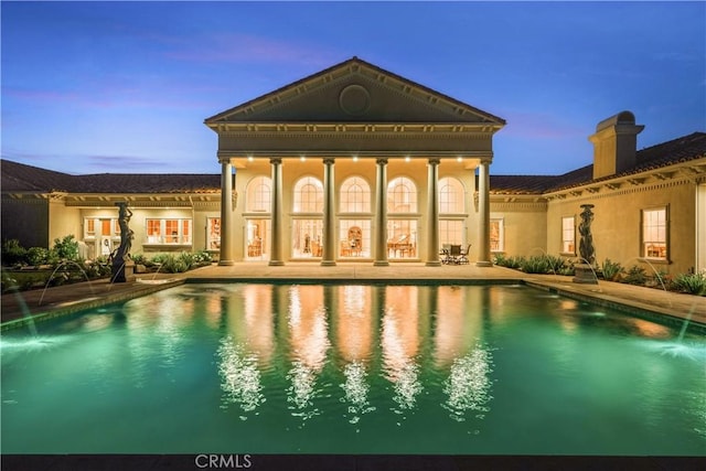 rear view of property with a chimney, stucco siding, and an outdoor pool