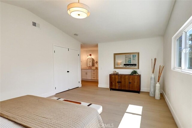 bedroom featuring visible vents, light wood-style floors, baseboards, and vaulted ceiling