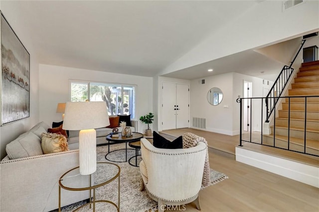 living area with visible vents, lofted ceiling, wood finished floors, and stairway