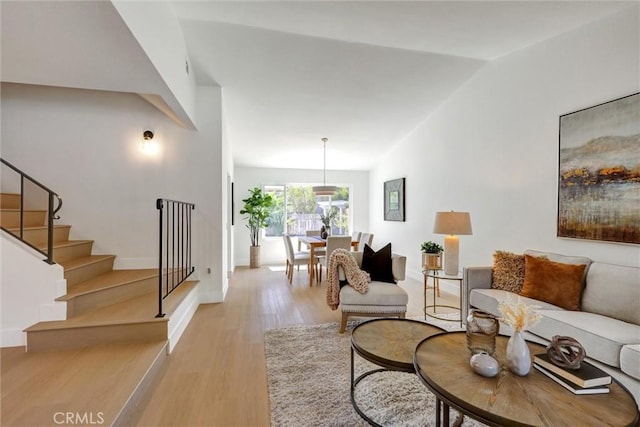 living area featuring stairs, baseboards, vaulted ceiling, and wood finished floors