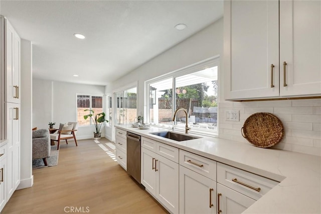 kitchen with backsplash, dishwasher, a sink, light countertops, and light wood-style floors