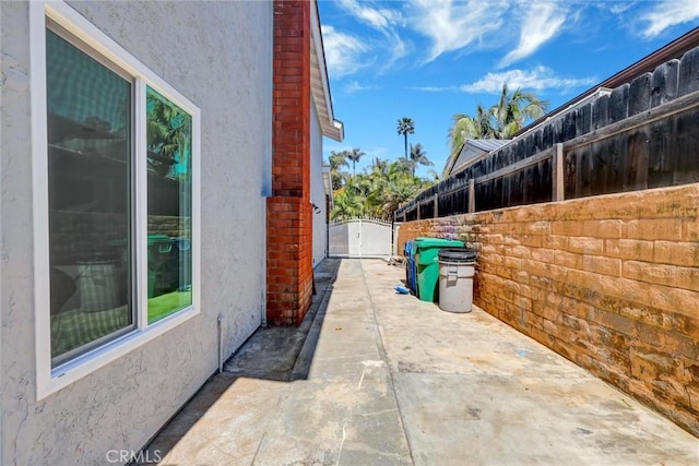 view of side of home featuring a patio, fence, a gate, and stucco siding