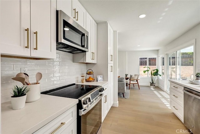kitchen featuring decorative backsplash, light countertops, white cabinets, light wood-style flooring, and stainless steel appliances