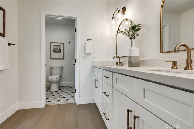bathroom featuring double vanity, wood finished floors, a sink, baseboards, and toilet