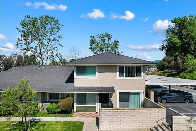 view of front of property featuring roof with shingles, covered and uncovered parking, and stucco siding