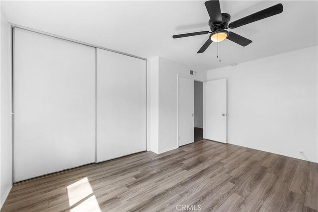 unfurnished bedroom with a ceiling fan, visible vents, wood finished floors, and a closet