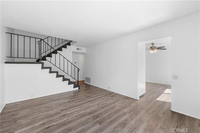 unfurnished living room featuring ceiling fan, stairs, wood finished floors, and visible vents