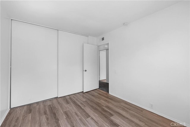 unfurnished bedroom featuring visible vents, wood finished floors, and a closet