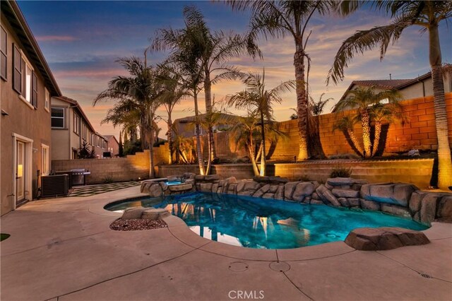 13744 Star Ruby Ave, Eastvale, CA 92880 - pool at dusk featuring a pool with connected hot tub, cooling unit, a fenced backyard, and a patio area