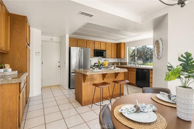kitchen featuring a breakfast bar area, light tile patterned floors, brown cabinets, visible vents, and black appliances