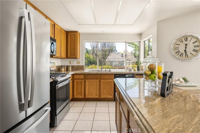 kitchen with stainless steel appliances, brown cabinets, light tile patterned flooring, and a sink
