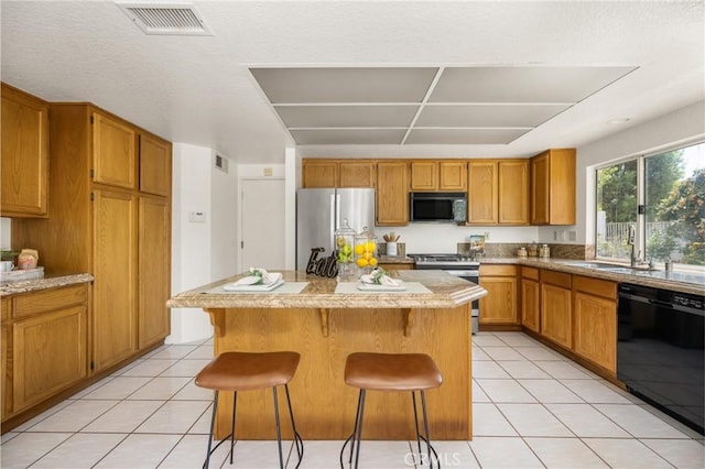 kitchen with light tile patterned flooring, a kitchen island, black appliances, and visible vents