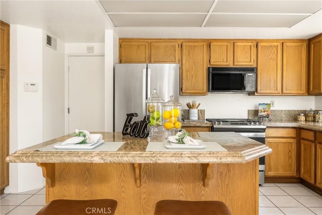kitchen featuring light tile patterned floors, stainless steel appliances, visible vents, and a kitchen bar