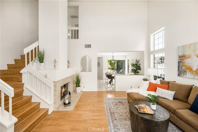 living room featuring wood finished floors, a fireplace, visible vents, a towering ceiling, and stairs