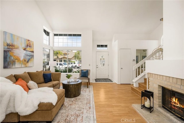 living room with stairway, light wood finished floors, a fireplace, and high vaulted ceiling