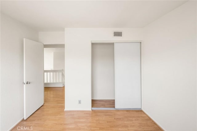 unfurnished bedroom with a closet, light wood-type flooring, visible vents, and baseboards