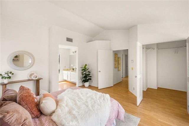bedroom with lofted ceiling, light wood-style floors, ensuite bath, and visible vents
