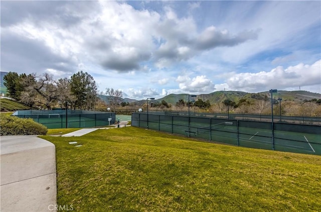 view of sport court featuring fence, a mountain view, and a lawn