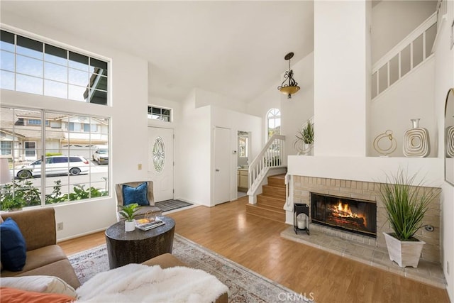 living area with stairs, a brick fireplace, high vaulted ceiling, and wood finished floors