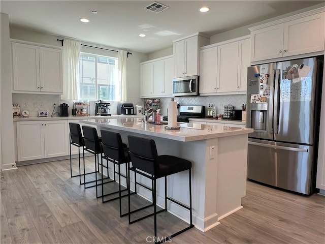 3530 E Delight Paseo Unit 205, Ontario, CA 91761 - kitchen featuring appliances with stainless steel finishes, decorative backsplash, a kitchen bar, light wood finished floors, and white cabinets