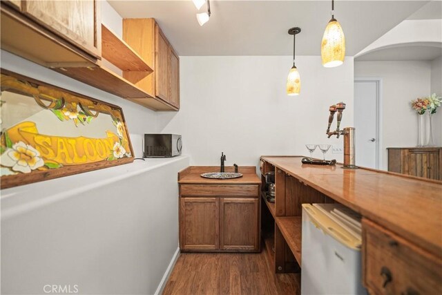 bar featuring arched walkways, dark wood finished floors, stainless steel microwave, baseboards, and pendant lighting