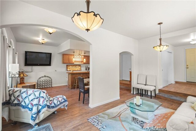 living area with baseboards, arched walkways, and wood finished floors