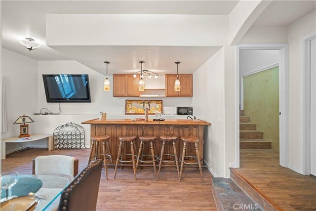 bar featuring black microwave, hanging light fixtures, stairs, and wood finished floors
