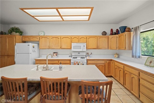 kitchen with a sink, white appliances, light countertops, an island with sink, and light tile patterned floors