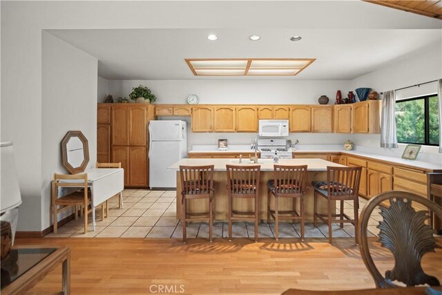 kitchen with a kitchen island with sink, white appliances, recessed lighting, light countertops, and a sink