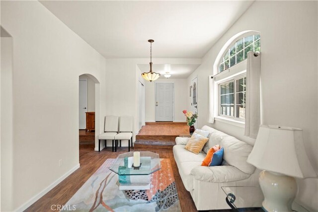 living room with dark wood-style flooring, arched walkways, and baseboards