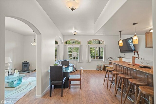 dining space with arched walkways, baseboards, wood finished floors, and a wood stove